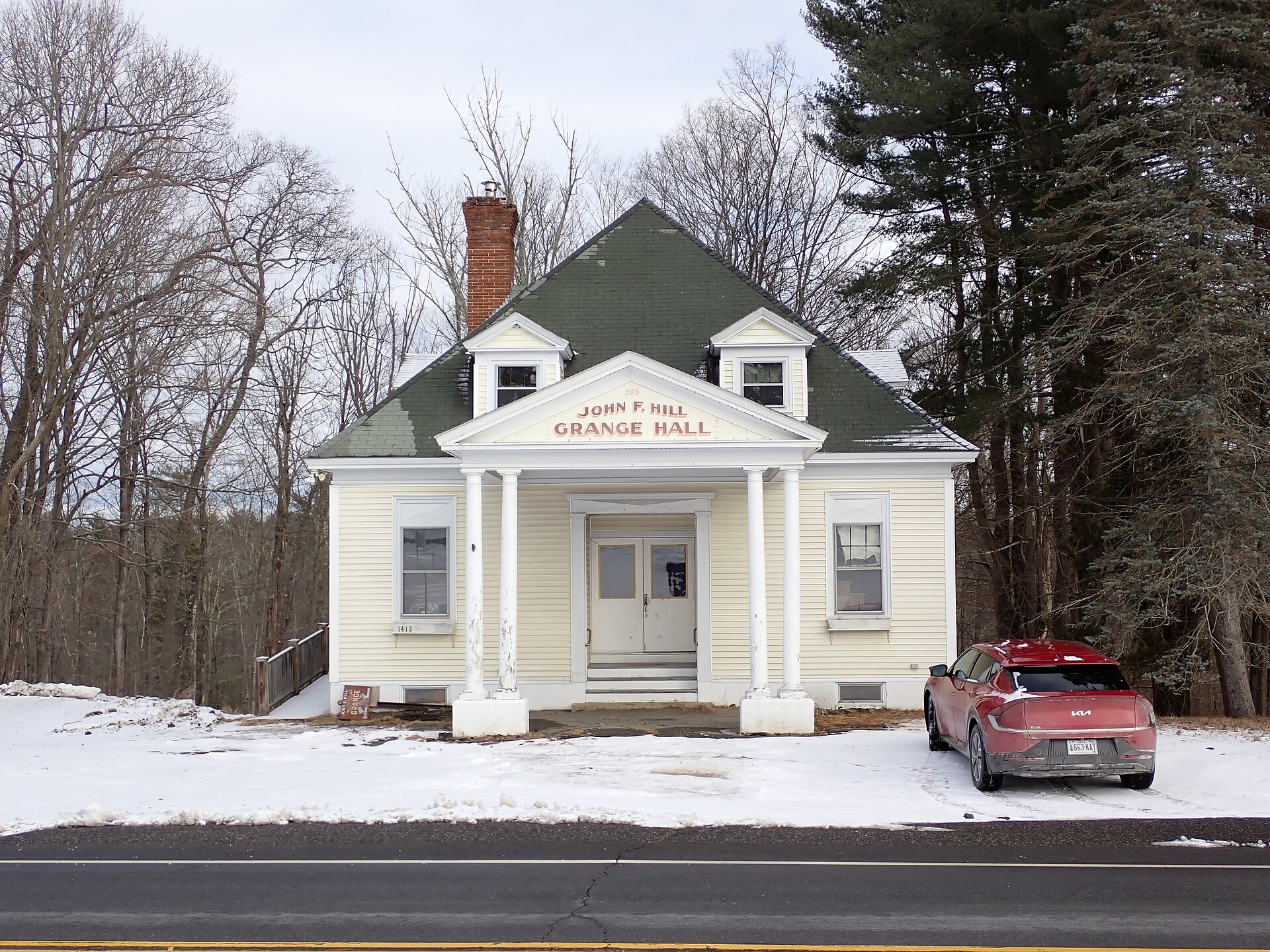 The John F. Hill Grange Hall in Eliot, Maine, a white clapboard hall with a green roof in the snow
