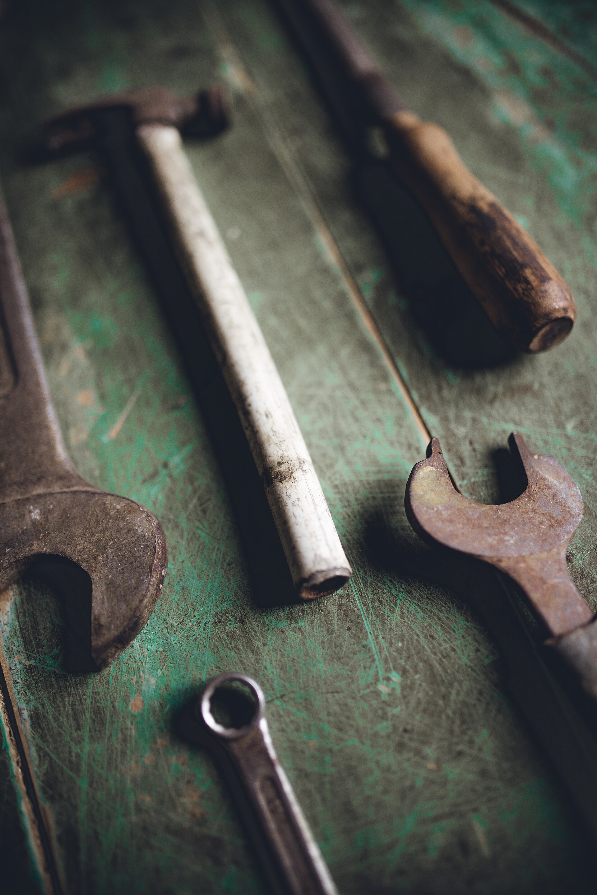 Wrenches and a hammer laid out on a weathered green workbench